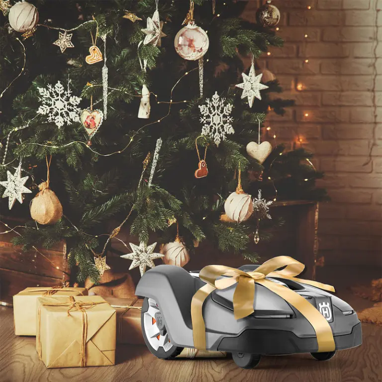 Ein Husqvarna Automower liegt als Geschenk verpackt und einem Weihnachtsbaum